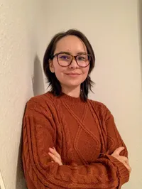 Humar Naman, Teilnehmerin des Young Talent Programms, steht an eine Helle Wand gelehnt und lächelt freundlich.